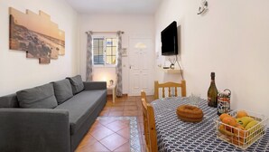 A small living area with a sofa, a dining table with a fruit basket, a television, and a painting on the wall. - Vacation Home "Las Arenas Bajo" close to the Sea with Wi-Fi (Las Arenas)