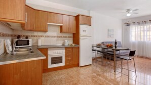 Una cocina compacta con armarios de madera, un microondas, un refrigerador, una mesa de comedor con sillas y un ventilador de techo.