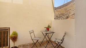 Un pequeño espacio al aire libre con una mesa, dos sillas, una planta en maceta y una ventana con rejas.