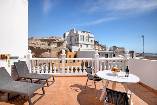 Une terrasse avec une table blanche, des chaises et une vue sur une falaise et des bâtiments.
