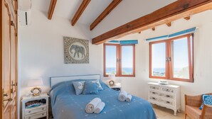 Un dormitorio con una cama grande, vigas de madera, una mesita de noche, un aparador y una ventana con vistas.