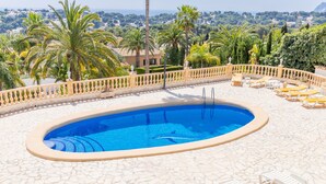 Una piscina con sillas de descanso, un solárium con baldosas y vistas a un pueblo.