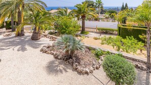 Un jardín con palmeras, un sendero de grava y vista al mar.