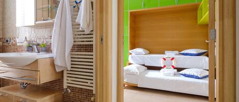Una habitación de hotel con baño, una cama con ropa de cama blanca, un adorno con un flotador de salvamento y un armario verde.