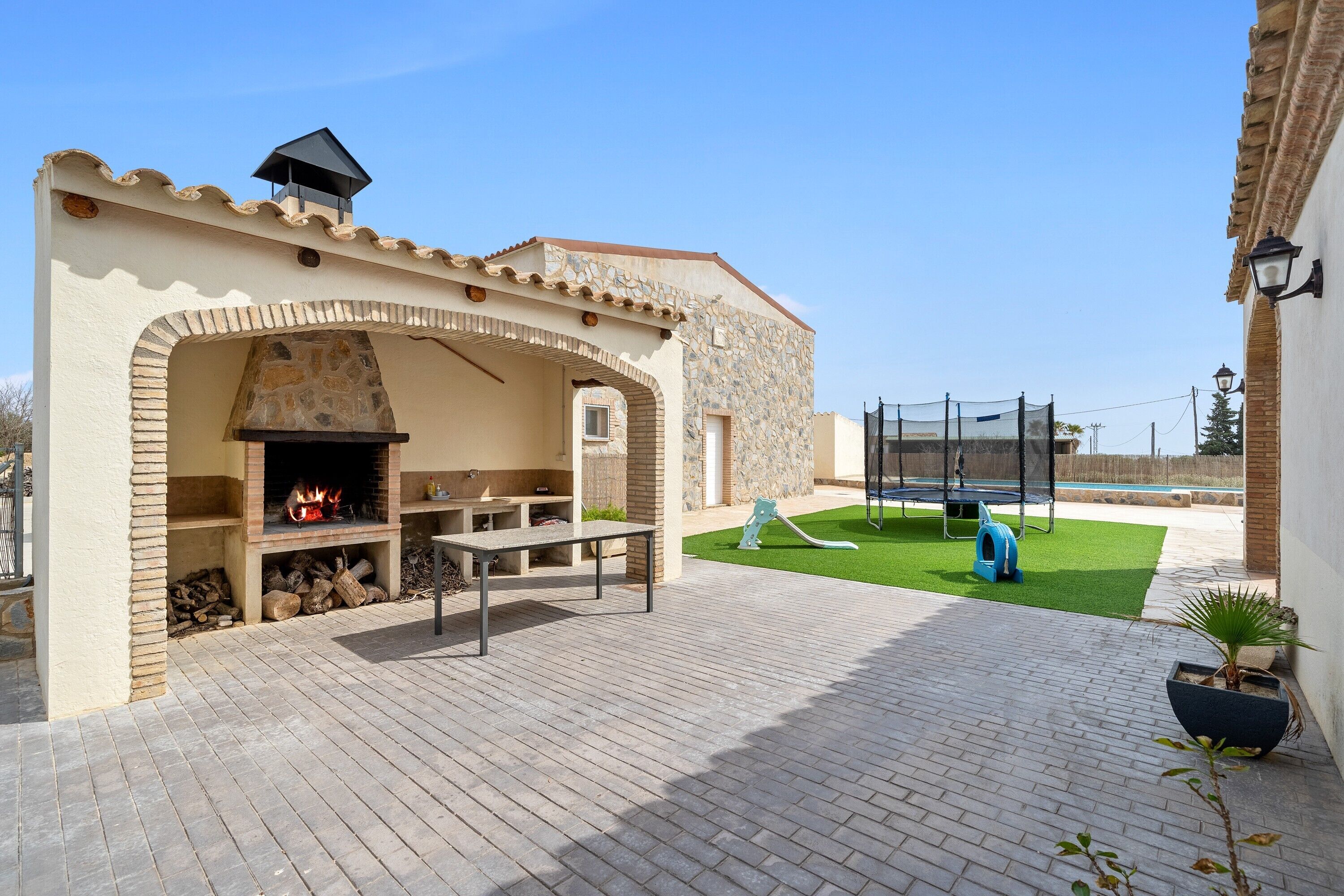 An outdoor patio with a stone fireplace, a table, and a small play area with a slide and a ball pit.
