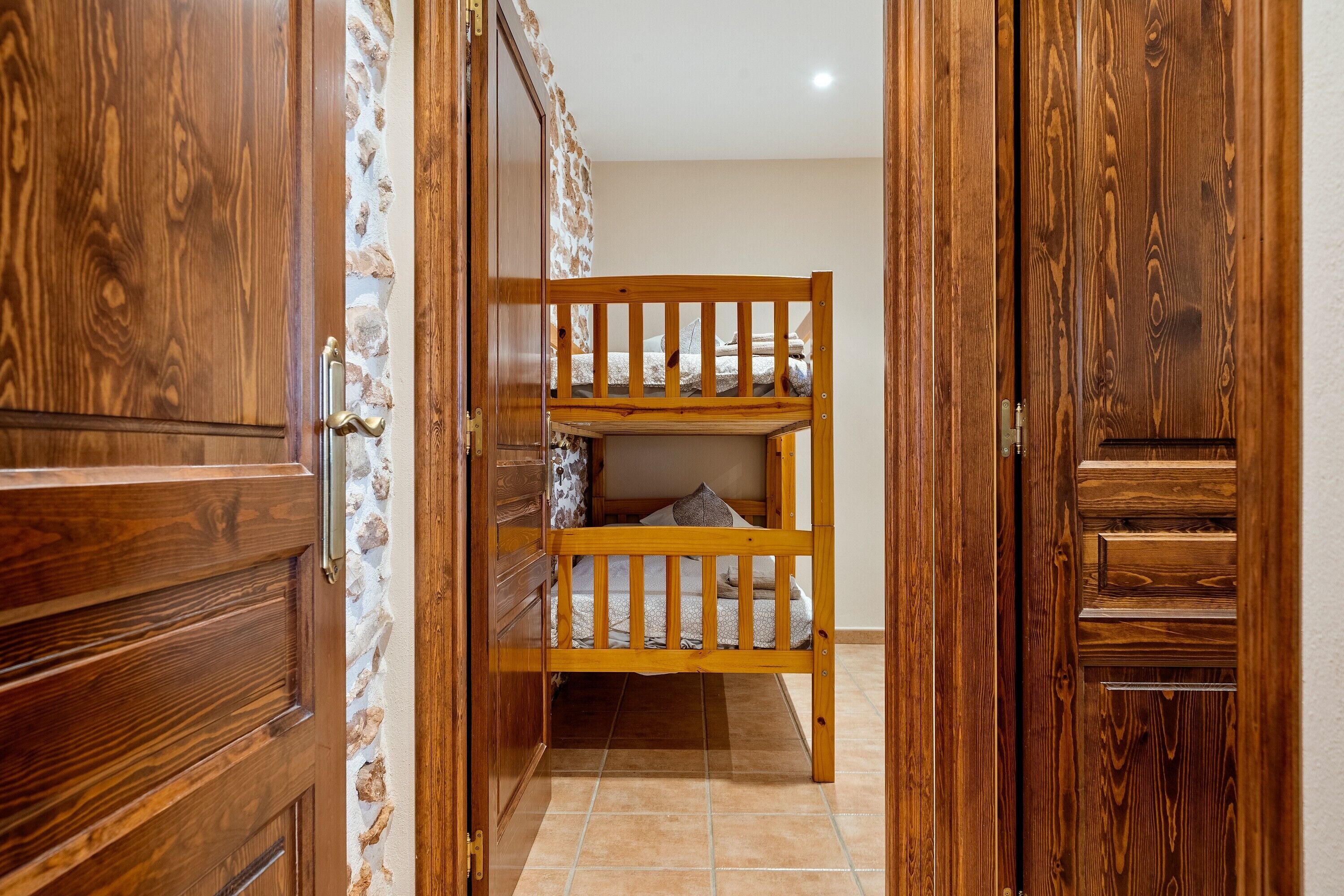 Una cama litera de madera en una habitación con un muro de piedra decorativo y puertas de madera.
