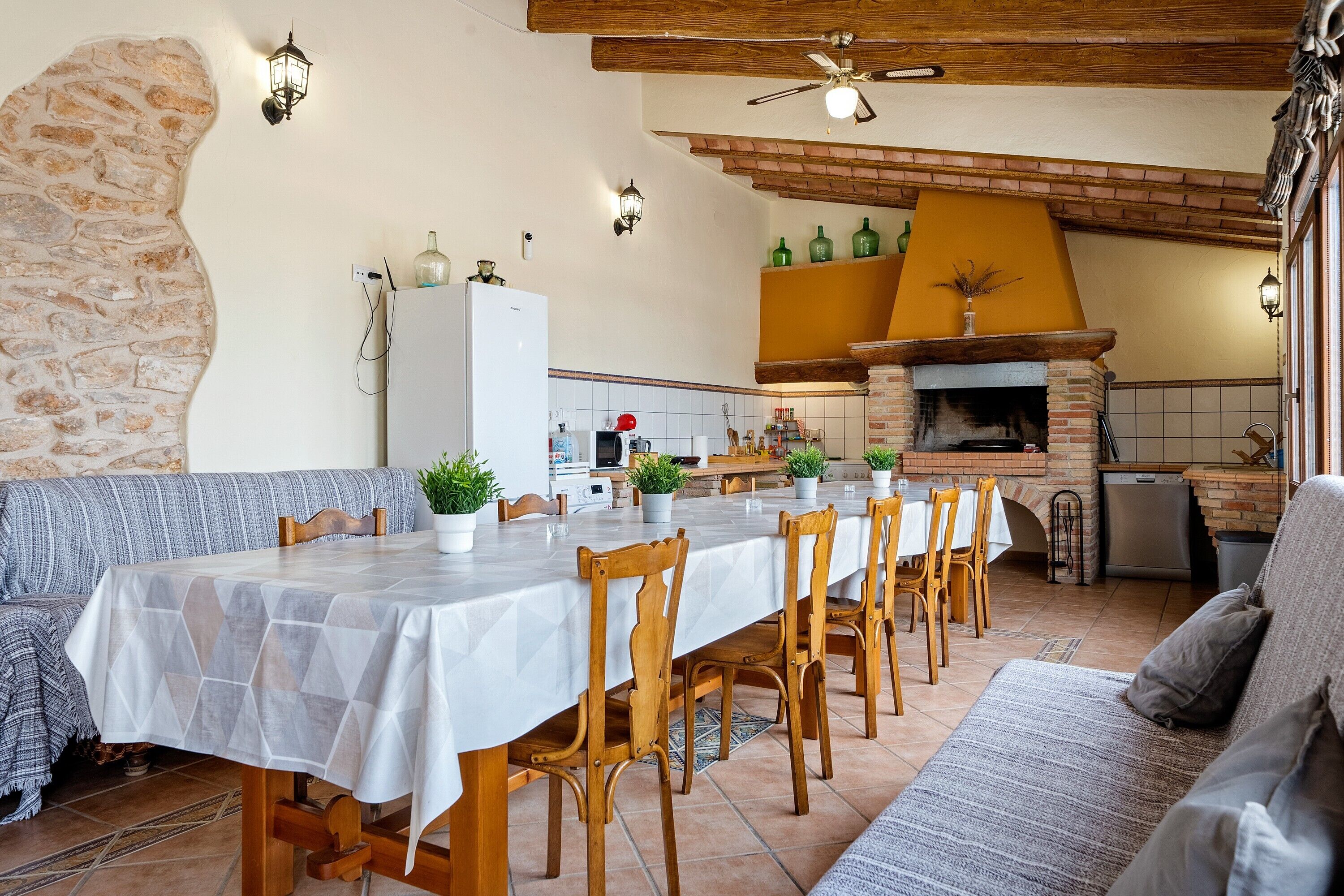 A dining area with a long table, wooden chairs, a brick fireplace, and a stone wall.
