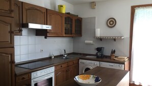 A kitchen with wooden cabinets, a stainless steel sink, a built-in oven, a washing machine, and a bowl on the counter. - Holiday Home "Pass Giraudière" with Terraces (LE GRAND VILLAGE PLAGE)