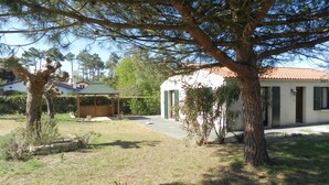A residential property with a covered outdoor seating area, a small house with a tiled roof, and a large tree in the foreground. - Holiday Home "Pass Giraudière" with Terraces (LE GRAND VILLAGE PLAGE)
