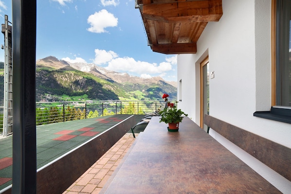 Un balcon avec vue sur les montagnes, une plante en pot et un banc en bois.