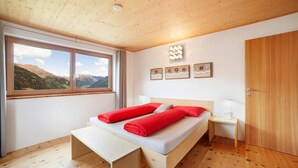A room with a bed, a window with a mountain view, a wooden ceiling, and a wooden door. - Apartment 'Joshof Talblick' with Mountain View, Private Terrace and Wi-Fi (Moso in Passiria)