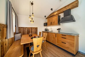 A wooden dining table with chairs, a kitchen with wooden cabinets, and pendant lighting.