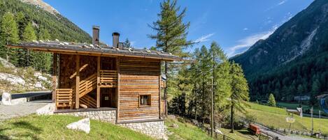 A wooden cabin with a staircase, a stone foundation, and a view of a mountainous landscape.