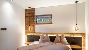 A modern bedroom with a wooden headboard, a bedside table, a window with a view, and a hanging light fixture. - Apartment "Grogg 608 I" with Mountain View, Garden & Wi-Fi (Martello)