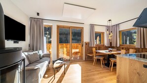 A modern living room with a flat-screen TV, a sofa, a dining area with a table and chairs, and a kitchen counter. - Apartment "Grogg 608 I" with Mountain View, Garden & Wi-Fi (Martello)