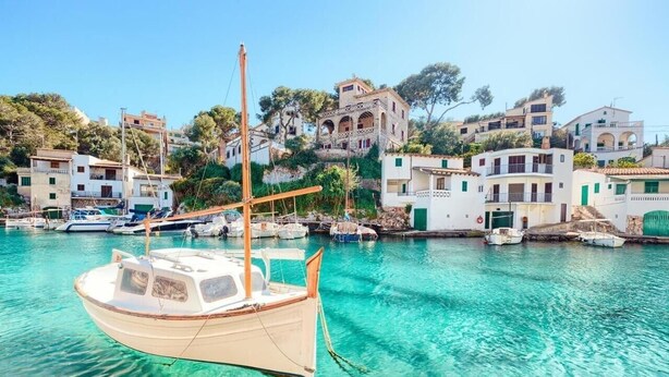Un puerto costero con barcos, edificios y mar azul cristalino.