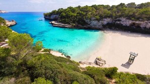 Paisaje costero con una playa, aguas turquesas cristalinas y acantilados rocosos.