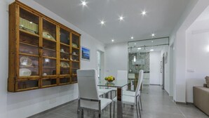 Un espace repas moderne avec une table en verre, des chaises blanches et un meuble en bois doté de portes en verre.