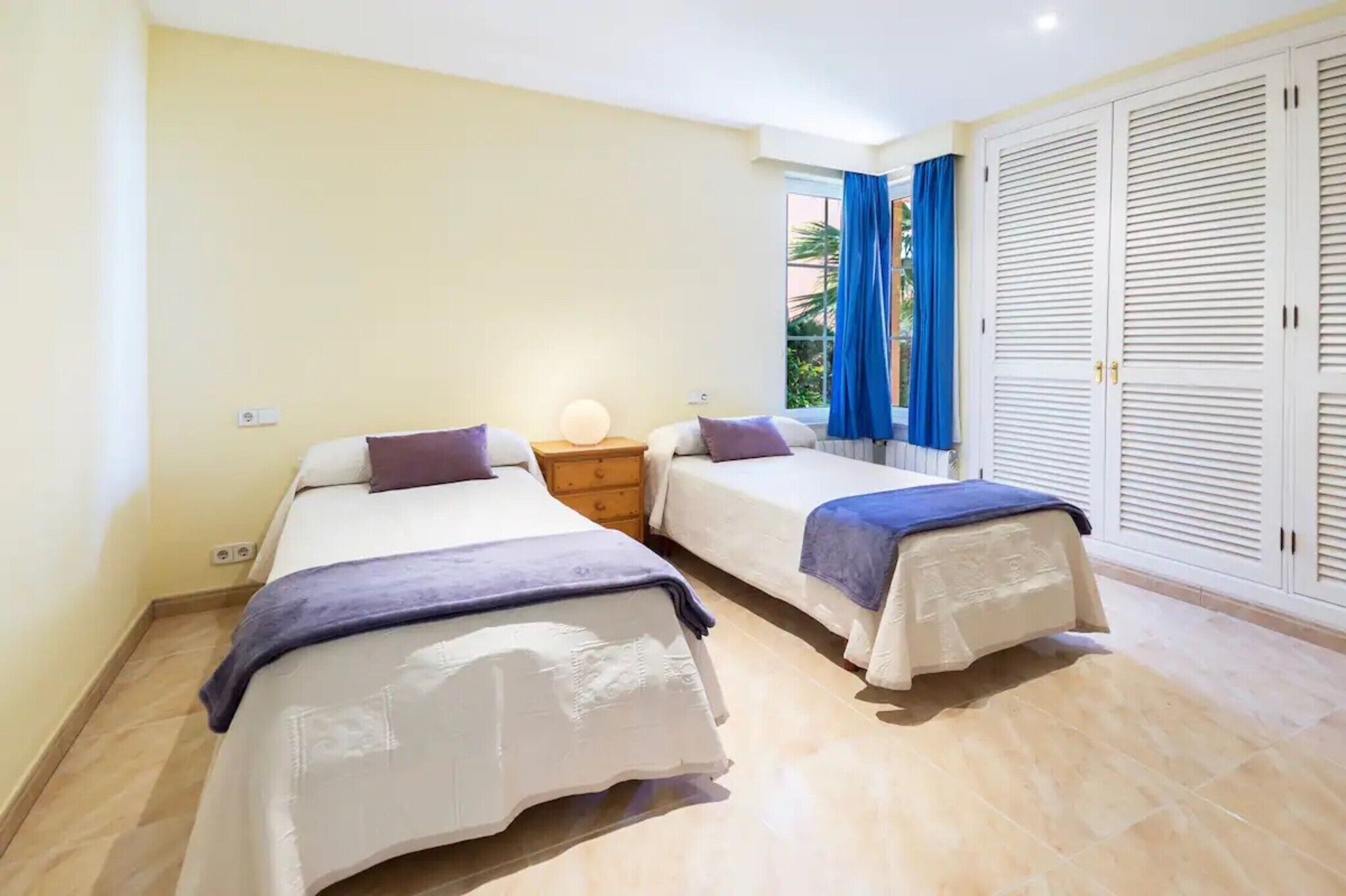 Une chambre avec deux lits, une table de chevet, une lampe et une armoire.