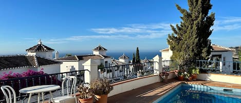 A rooftop swimming pool with a view of the sea, surrounded by white buildings with tiled roofs.