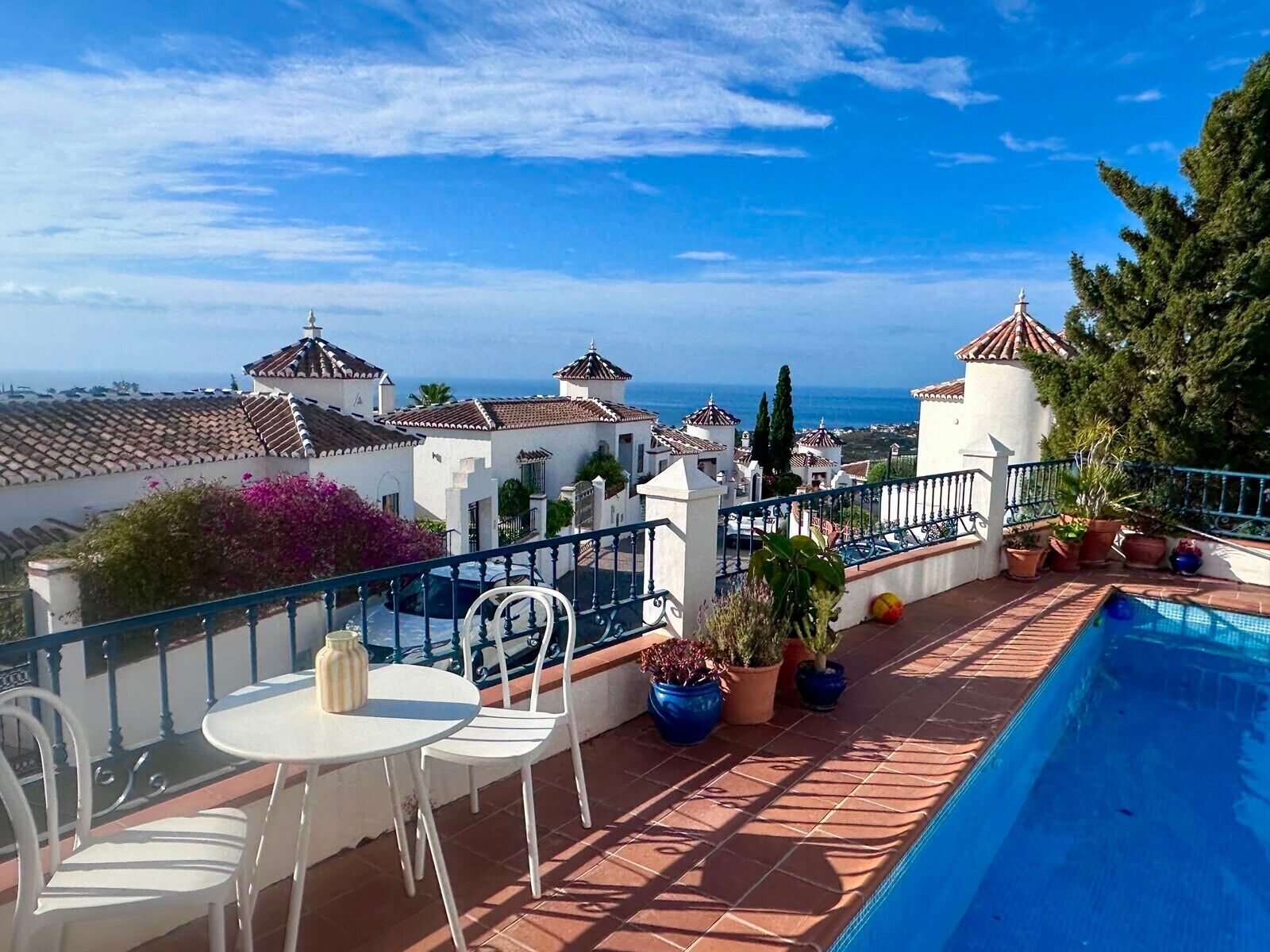 A rooftop terrace with a pool, white chairs, and potted plants.