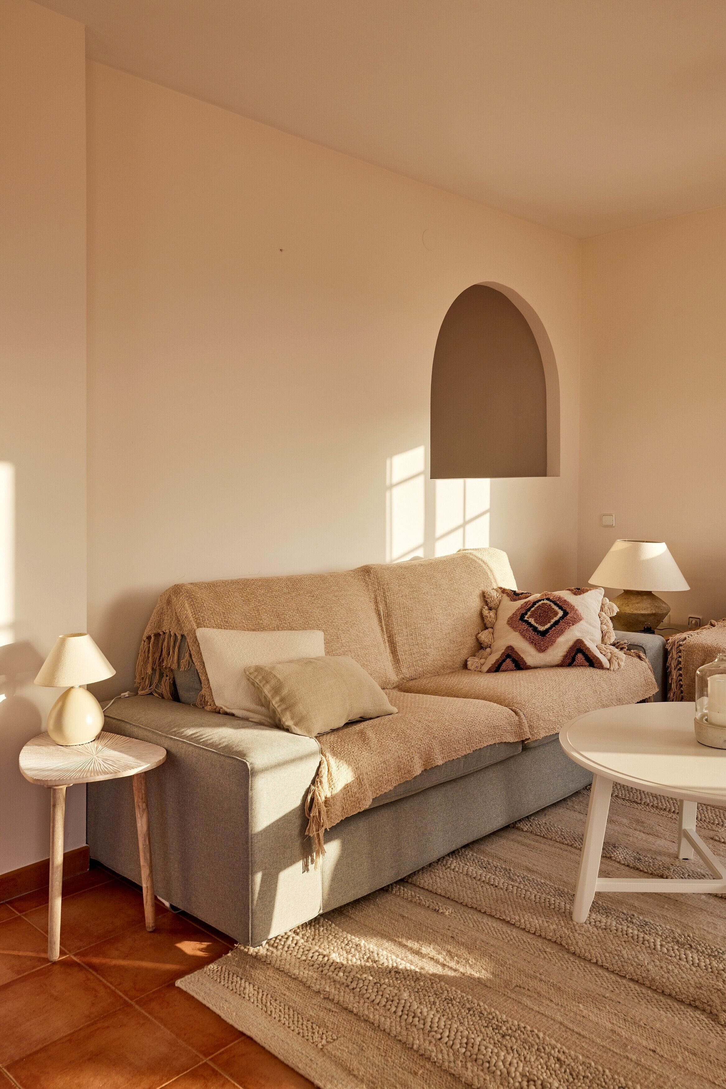 A cozy living room with a sofa, two side tables, a lamp, and a round coffee table.