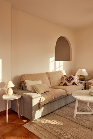 Un salon chaleureux avec un canapé, deux tables d’appoint, une lampe et une table basse ronde.