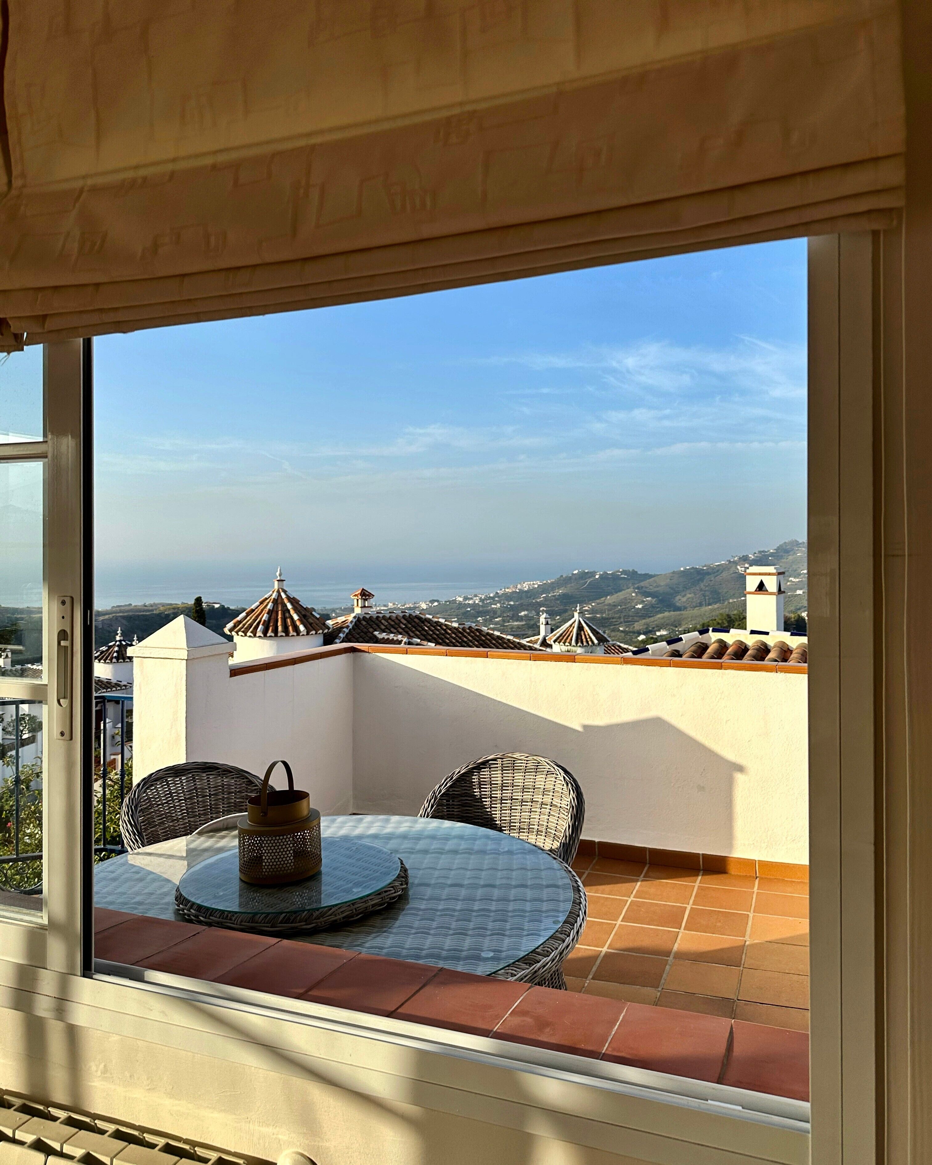 Un balcon avec une table et des chaises, une vue sur la mer et un paysage lointain.