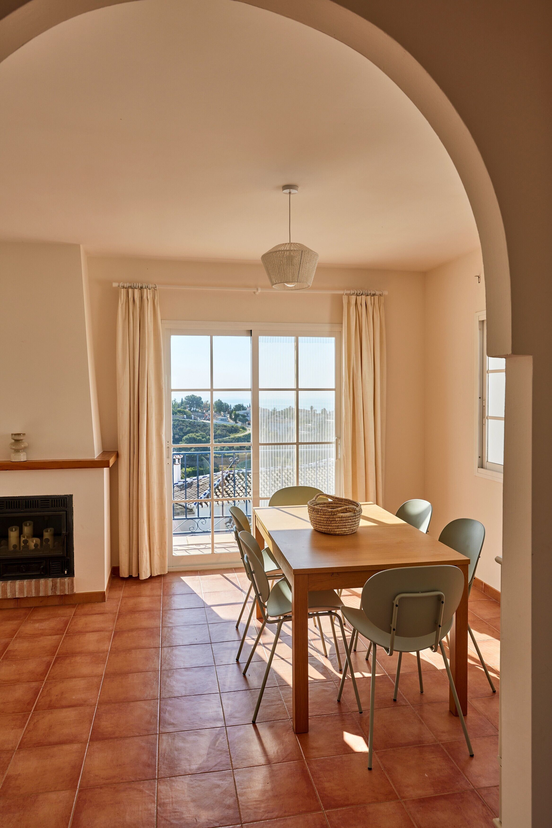 A dining area with a table, chairs, a fireplace, and a view through large windows.