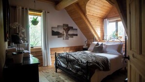 Une chambre confortable avec un plafond en pente, un lit avec un cadre en métal, une table de chevet avec une lampe et une fenêtre avec des rideaux.