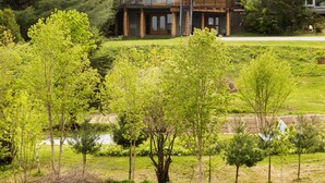 Une grande cabane en rondins dotée d’un balcon, entourée d’une végétation luxuriante et bordée d’un lac.