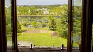 Une porte en bois ouverte donne sur un balcon d’où l’on peut admirer un lac, des arbres et des bâtiments au loin.