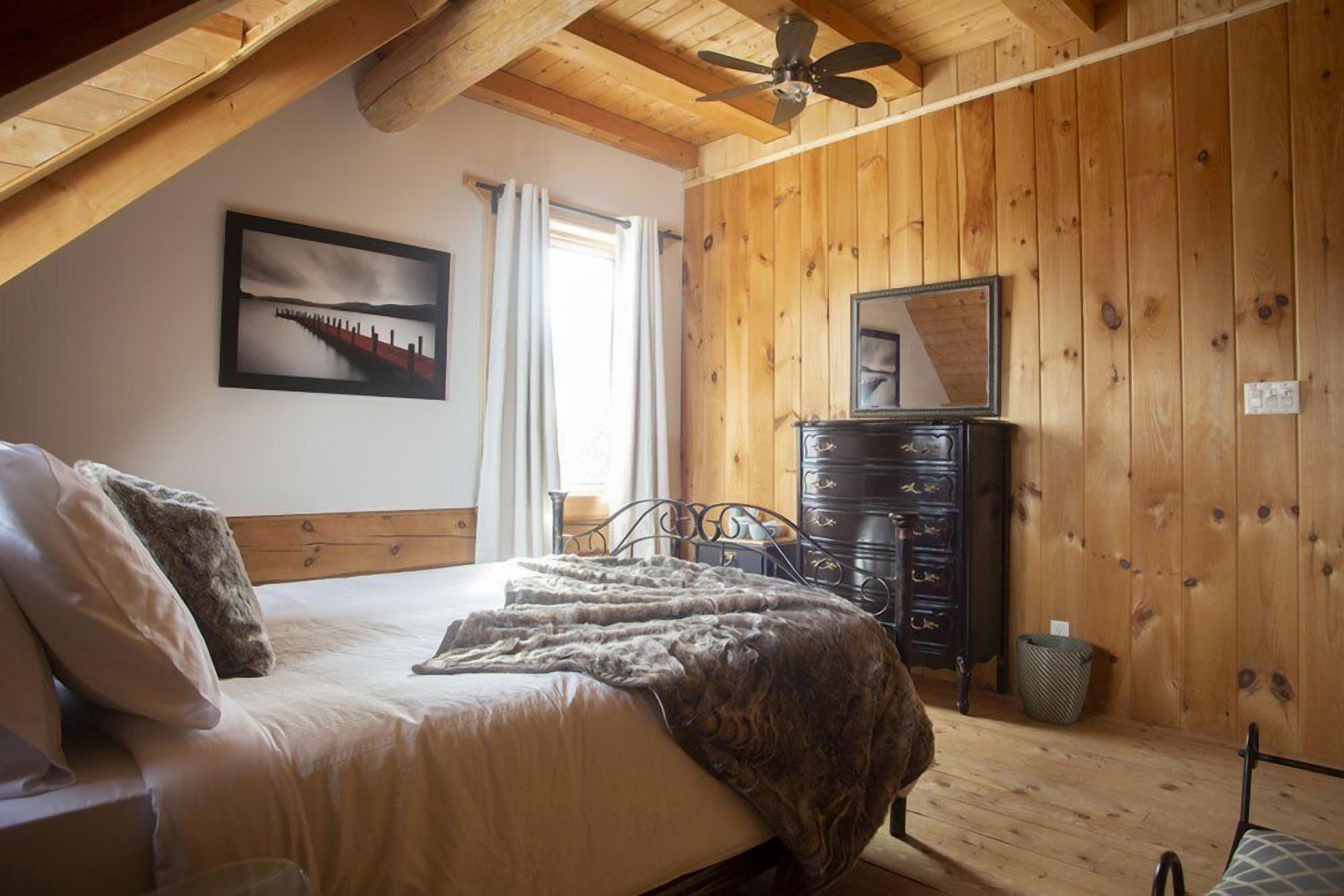 A bedroom with a wooden ceiling, a bed with a blanket, a dresser, a mirror, and a picture on the wall.