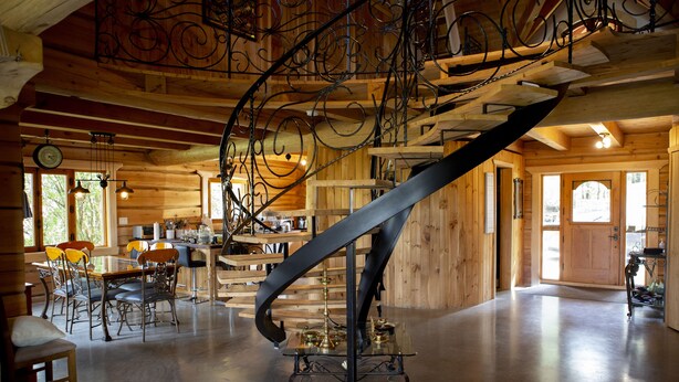Un escalier en colimaçon dans un intérieur en bois, avec un espace repas et une cuisine visibles.