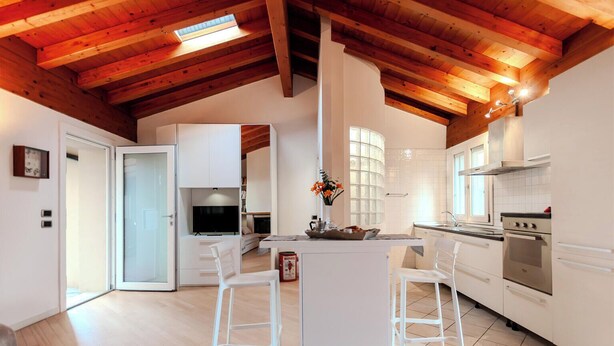 Una cocina moderna con vigas de madera, armarios blancos y una isla central con taburetes de bar.