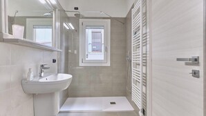 Un baño moderno con un lavamanos pedestal, una ducha con puerta de cristal y un perchero para toallas.