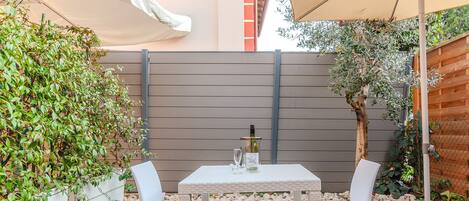 Eine Terrasse mit Tisch und Stühlen, einer Weinflasche und einem weißen Sonnenschirm.