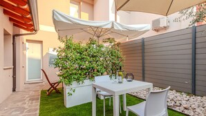 Un patio exterior con una mesa, sillas, un paraguas blanco y una maceta con follaje verde.
