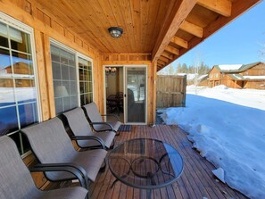 En træterrasse med udendørs møbler og et glasbord, omgivet af sne.