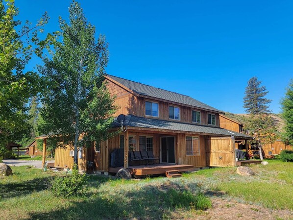 Une cabane en bois à deux étages, dotée d’un porche, entourée d’arbres et surplombant un ciel dégagé.