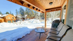 A covered outdoor seating area with a table and chairs, a wooden deck, and a view of snow-covered houses and trees. - Sunshine Station - 3 bedroom Winthrop Townhouse (Winthrop)