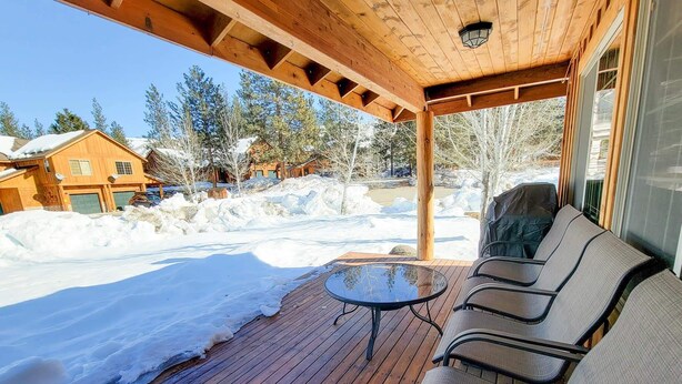 Un espace extérieur aménagé, abrité, avec une table et des chaises, une terrasse en bois et une vue sur des maisons et des arbres recouverts de neige.