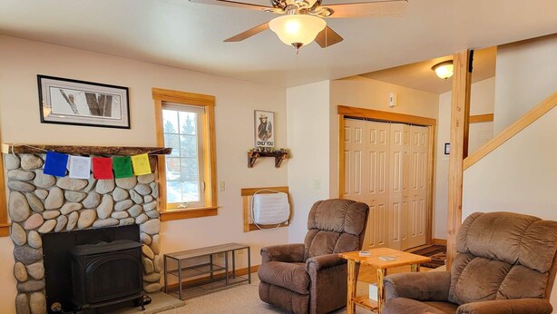 A cozy living room with a stone fireplace, a ceiling fan, a comfortable sofa, and a wooden table. - Sunshine Station - 3 bedroom Winthrop Townhouse (Winthrop)