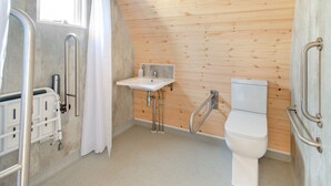 Un baño con pared de madera, un lavamanos blanco, un inodoro y una zona de ducha.