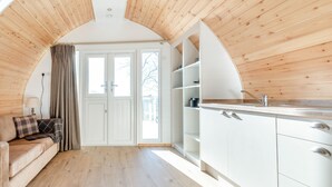 Een moderne keuken met witte kasten en een houten plafond, een beige bank met een ruitkussen, en een groot raam met gordijnen.