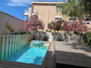 A swimming pool with a wooden deck, surrounded by a low wall and flowering plants.