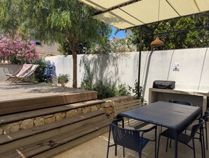 Eine Terrasse im Freien mit Tisch, Stühlen, einem Grill und einer überdachten Sitzgelegenheit.
