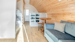 A cozy room with a wooden ceiling, a blue sofa, a small wooden table, and a white cabinet with kitchenware. - Carlton Manor Pod 8 (Hull)