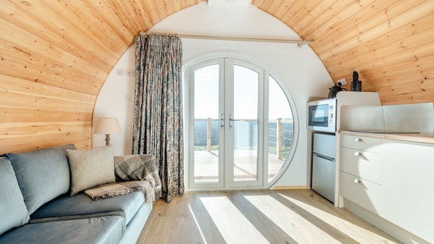 A cozy cabin interior with a wooden ceiling, a sofa, a dining area, and a large glass door leading to a balcony. - Carlton Manor Pod 8 (Hull)