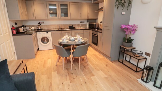 Une cuisine moderne avec des meubles gris, un lave-linge et un coin repas avec une table dressée pour quatre personnes.